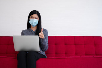 亚洲女人穿脸面具和使用移动PC的沙发为工作从首页和拇指<strong>新生活方式</strong>正常的在检疫概念保持首页