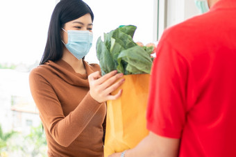 亚洲女人穿脸面具和皮卡购物袋新鲜的食物蔬菜和水果从交付男人。从超市概念表达杂货店服务和新生活方式