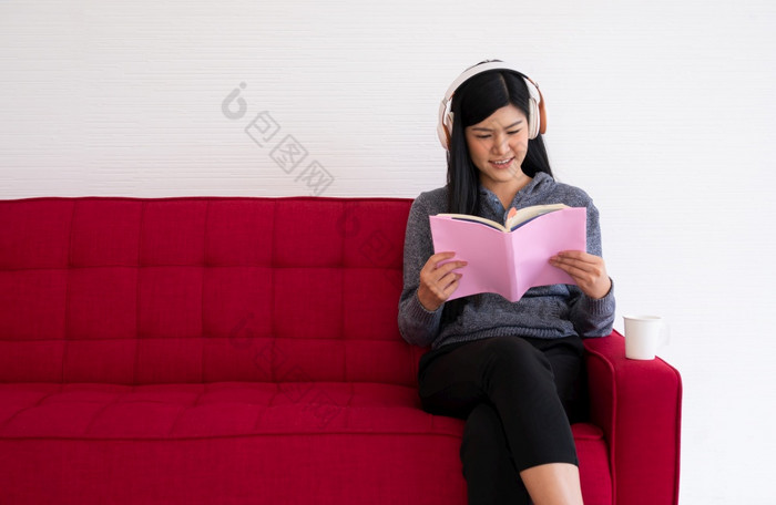 可爱的亚洲女人坐着的沙发的早....和阅读书而听音乐的生活房间