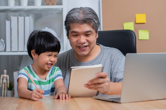 亚洲父亲工作的首页办公室与移动PC和教学家庭作业与女儿新生活方式正常的在检疫概念保持首页自由和为父之道概念
