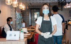 亚洲女服务员女人穿脸面具和持有红外额头温度计检查身体温度为病毒症状客户之前进入的餐厅咖啡商店