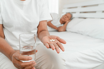 老上了年纪的女人持有医学和水手的床上的卧室和她的丈夫睡觉旁边概念睡眠问题的上了年纪的和使用镇静剂和睡眠医学上瘾