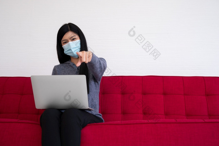 亚洲女人穿脸面具和使用移动PC的沙发为工作从首页和点向前新生活方式正常的在检疫概念保持首页