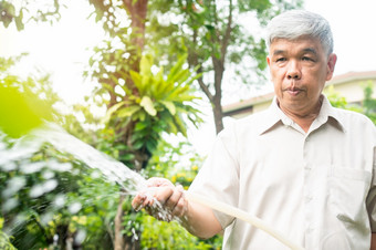 快乐和微笑亚洲老上了年纪的男人。浇水植物和花为爱好后退休首页概念快乐生活方式和好健康为老年人