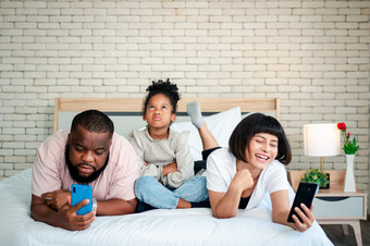 非洲美国女孩是不满意和伤心坐着的中间之间的父亲和妈妈。<strong>父母</strong>是使用的智能手机和被遗弃的孩子们孩子们需要他们的<strong>父母</strong>注意