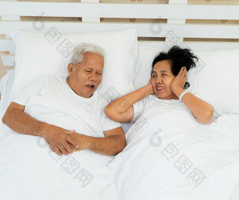 老亚洲女人铺设开放她的眼睛和封面耳朵与她的手床上旁边她的丈夫谁<strong>鼾声</strong>和使噪音婚姻问题