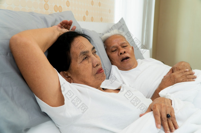 老亚洲女人铺设开放她的眼睛床上旁边她的丈夫谁鼾声和使噪音婚姻问题