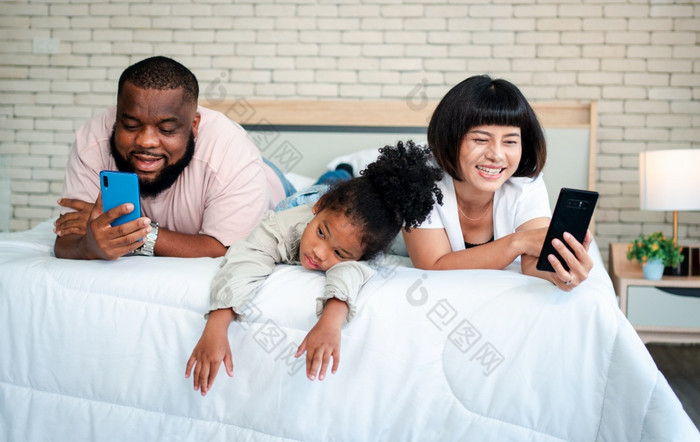 非洲美国女孩是不满意和伤心坐着的中间之间的父亲和妈妈。父母是使用的智能手机和被遗弃的孩子们孩子们需要他们的父母注意