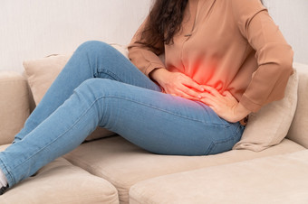 不开心亚洲女人坐着的沙发和持有胃痛苦腹部疼痛那来了从月经腹泻消化不良病和医疗保健概念