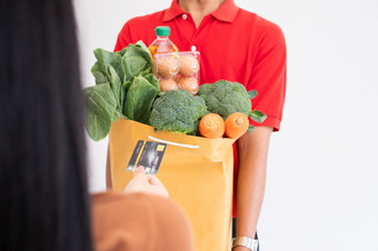 亚洲交付男人。从超市穿脸面具和持有袋新鲜的食物蔬菜和水果为给客户首页概念表达杂货店服务和新生活方式