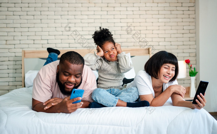 非洲美国女孩是不满意和伤心坐着的中间之间的父亲和妈妈。父母是使用的智能手机和被遗弃的孩子们孩子们需要他们的父母注意