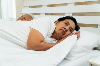 老亚洲女人铺设开放她的眼睛床上旁边她的丈夫谁鼾声和使噪音婚姻问题