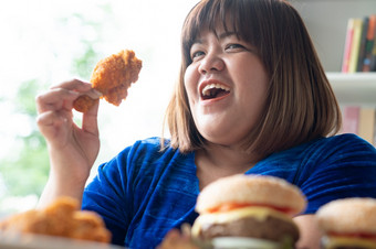 饿了超重女人持有炸鸡汉堡木板和披萨表格在工作从首页获得重量问题概念暴吃障碍床上