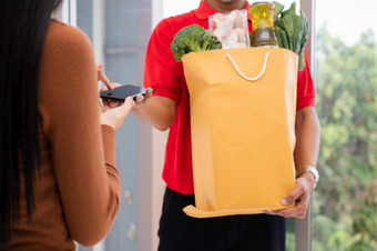 亚洲交付男人。持有持有袋新鲜的食物为给客户和持有智能手机为收到支付首页概念表达杂货店服务和新生活方式