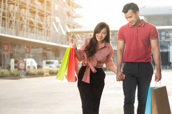 快乐年轻的夫妇购物者走的购物街对和持有色彩斑斓的购物袋手概念出售和黑色的星期五购物