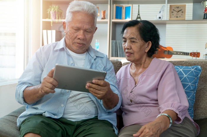 快乐亚洲高级夫妇使用的平板电脑为找到假期目的地的假期季节概念快乐上了年纪的生活方式后退休