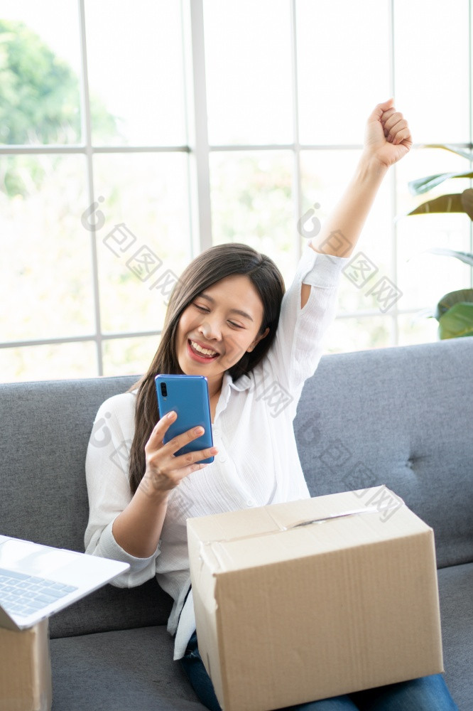 快乐年轻的亚洲女人企业家微笑为销售成功后检查订单从在线购物商店智能手机首页办公室概念商人业务在线和电子商务