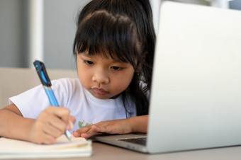 亚洲女孩学生持有笔为采取笔记和做家庭作业和使用的移动PC为在线学习类首页教育和距离学习为孩子们在家教育概念