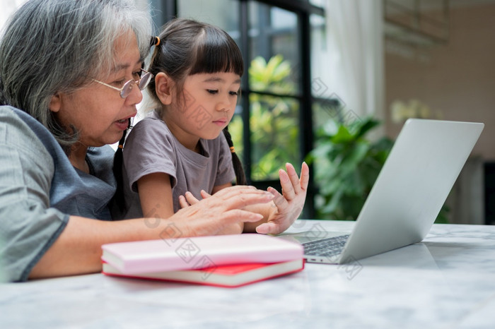 亚洲祖母与她的两个孙子有有趣的和玩教育游戏在线与电脑笔记本首页的生活房间概念在线教育和有爱心的从父母