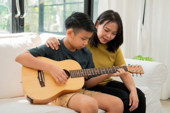 亚洲妈妈。拥抱儿子亚洲男孩玩吉他和妈妈。拥抱的沙发和感觉欣赏和鼓励概念快乐家庭学习和有趣的生活方式<strong>爱家</strong>庭关系