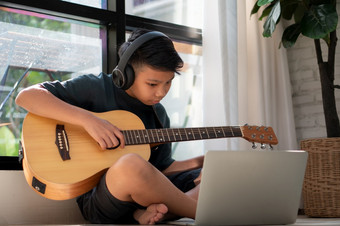 亚洲<strong>男</strong>孩玩吉他和看在线课程移动PC而练习为学习音乐音乐的仪器在线首页<strong>男</strong>孩学生研究在线与视频调用<strong>老师</strong>玩吉他
