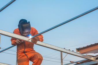 工人焊接橙色工作衣服焊接为屋顶桁架
