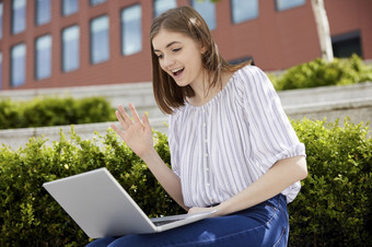 年轻的女大学<strong>学生</strong>办公室工人与移动PC有视频闲谈，<strong>聊天</strong>在户外大学校园