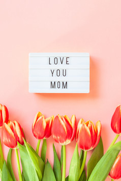 有创意的平躺前视图母亲一天问候卡与红色的郁金香春天花粉红色的背景庆祝活动明信片模板