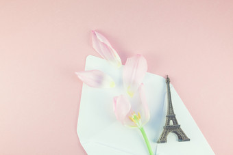 粉红色的郁金香与花瓣打开纸信封信与埃菲尔铁塔塔微型粉红色的背景平躺前视图浪漫的爱记忆概念