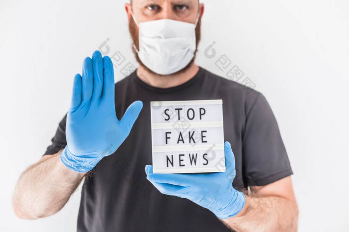 假的新闻infodemics在新冠病毒流感大流行概念男人。穿保护面具和医疗手套手持有lightbox与文本停止假的新闻人想要知道真理关于冠状病毒