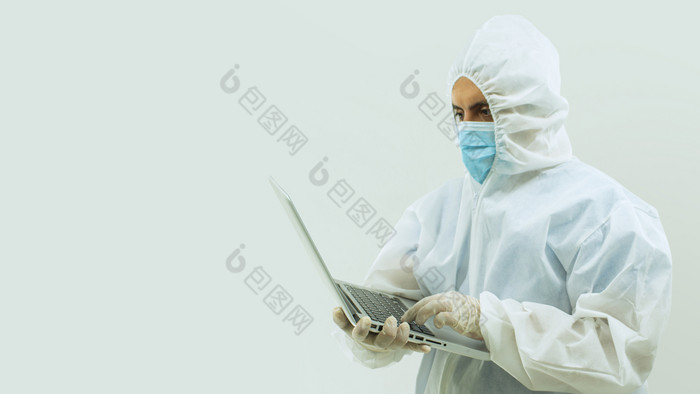 医生白色bioprotective西装和蓝色的面具站持有与他的手开放移动PC白色背景医生bioprotective西装和蓝色的面具站持有与他的手开放移动PC白色背景