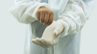 医生与面具和白色bioprotective西装把乳胶手套手的前景白色背景医生与面具和bioprotective西装把乳胶手套手的前景白色背景