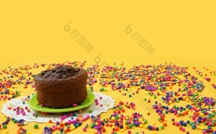 巧克力蛋糕小绿色板包围糖果球分散黄色的背景的蛋糕位于的左一边的照片巧克力蛋糕小绿色板包围糖果球分散黄色的背景图像与复制空间
