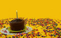 巧克力生日蛋糕与蓝色的和白色蜡烛基斯小绿色板包围糖果球分散黄色的背景图像与复制空间