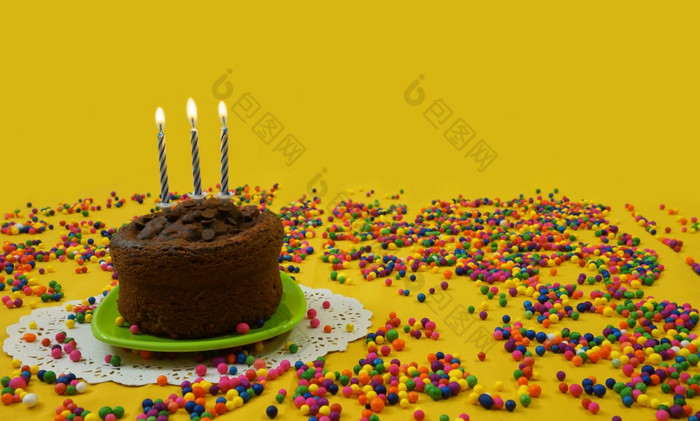 巧克力生日蛋糕与蓝色的和白色蜡烛基斯小绿色板包围糖果球分散黄色的背景图像与复制空间