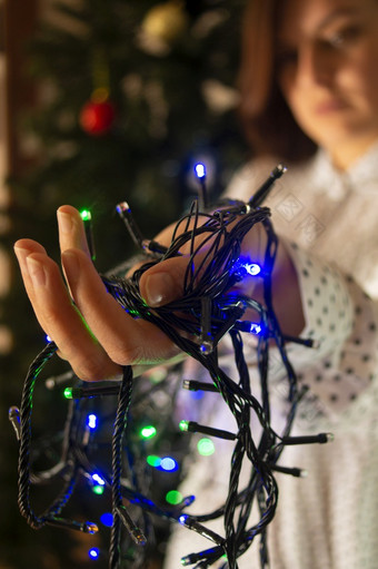 特写镜头女人手与红色的绿色和蓝色的彩色的灯装修的圣诞节树特写镜头女人手与彩色的灯装修的圣诞节树