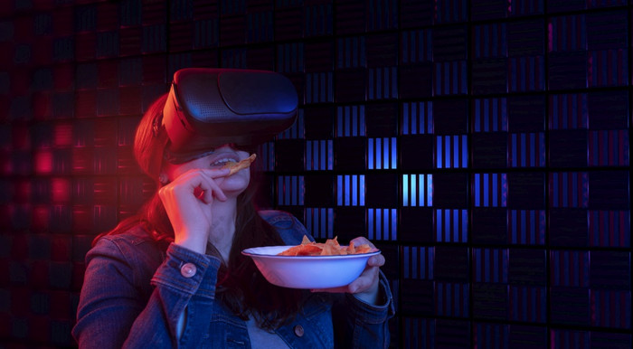拉美裔女人与虚拟现实护目镜与数字技术看电影网络空间与蓝色的和红色的光而吃玉米片拉美裔女人与虚拟现实护目镜与数字技术看电影网络空间与蓝色的和红色的光