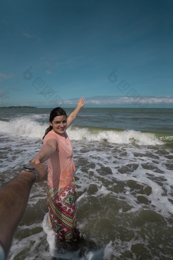 美丽的快乐年轻的拉美裔女人持有她的合作伙伴rsquo手的海滩穿粉红色的衣服与的海的背景在阳光明媚的早....美丽的快乐年轻的拉美裔女人持有她的合作伙伴rsquo手的海滩穿粉红色的衣服在阳光明媚的早..