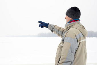 男人。与羊毛帽<strong>防水</strong>夹克和羊毛帽指示某物与的手指关闭的第聂伯河河在冷和伤心灰色的冬天早....下的雪