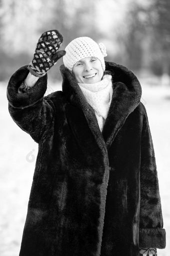冬天肖像微笑高级成人女人穿羊毛帽围巾和彩色的手套耶和华见证人与她的手与雪背景