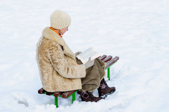 <strong>女</strong>人坐着板凳上和阅读书冬天雪