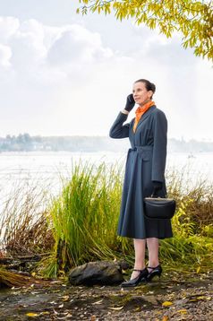 优雅的高级业务女人与移动电话袋和橙色围巾走沿着的河下的树秋天