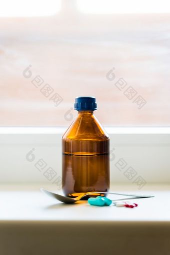 咳嗽糖浆瓶与勺子和一些药片关闭的窗口