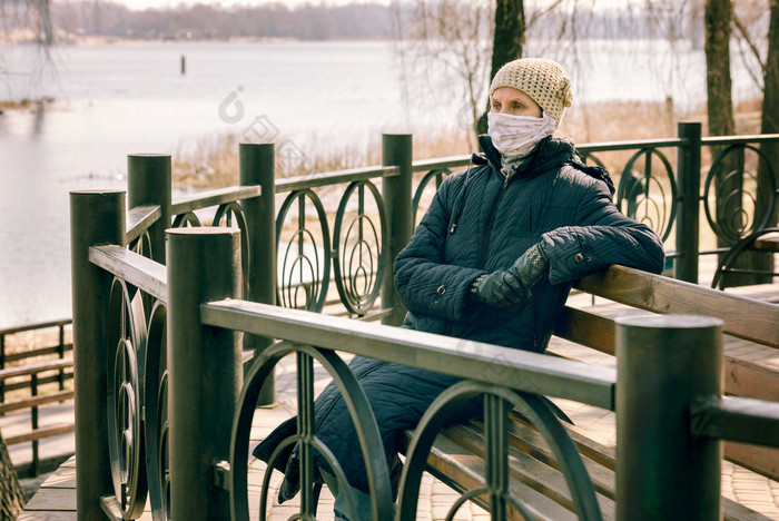 可怜的上了年纪的女人穿自制的面具保护自己从病毒这样的冠状病毒也已知的新冠病毒“非典”和步态她坐在板凳上关闭的河