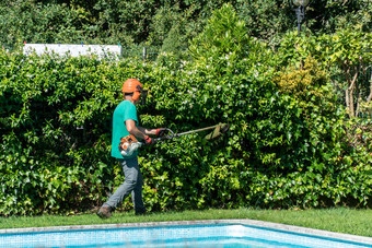 男人。装备与刷刀作品前面院子里与游泳池花园维护概念