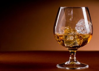 照片美味的玻璃白兰地威士忌与冰多维数据集棕色（的）背景