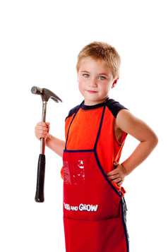 可爱的年轻的男孩持有重责任锤而且穿橙色围裙与口袋为工具孤立的