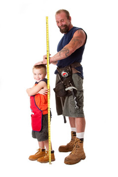 父亲穿工具带与玩具锤而且测量磁带措施高度可爱的儿子穿着橙色围裙孤立的