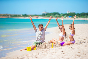 家庭爸爸和孩子们玩与沙子热带海滩父亲和孩子们使沙子城堡热带海滩家庭玩与海滩玩具