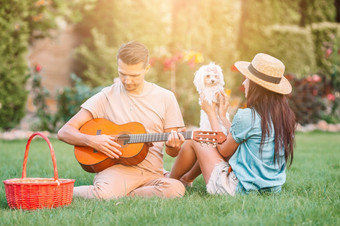 夫妇放松夏天野餐男人。持有的吉他和女人与白色小狗年轻的夫妇旅游享受夏天假期